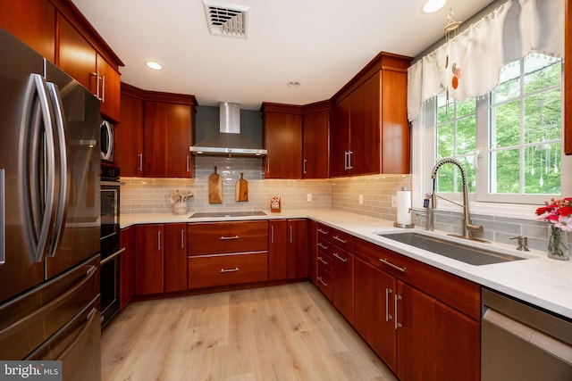 kitchen with black appliances, wall chimney exhaust hood, a sink, light wood-type flooring, and tasteful backsplash