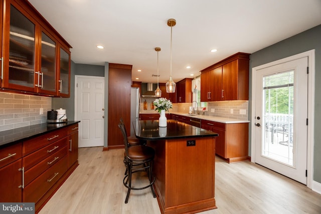 kitchen with light wood-style floors, decorative backsplash, a sink, decorative light fixtures, and a center island