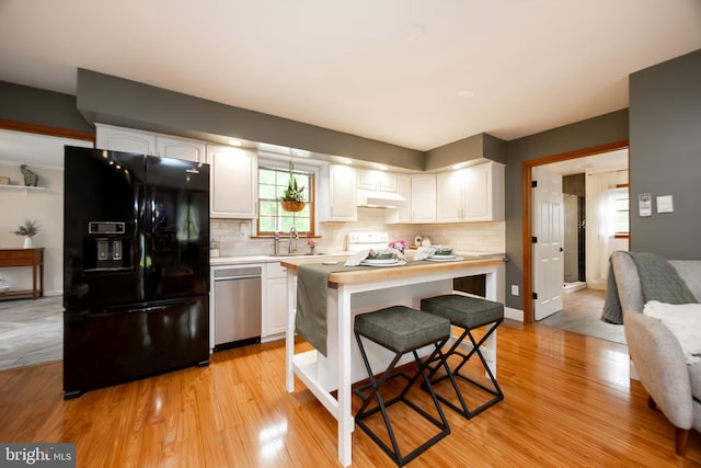 kitchen featuring black refrigerator with ice dispenser, under cabinet range hood, and white cabinetry