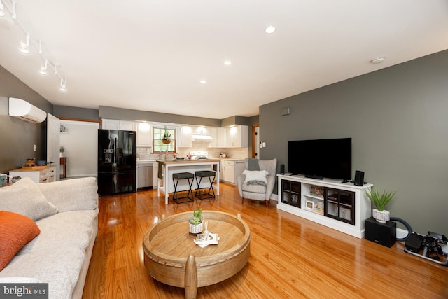 living area with a wall unit AC, light wood-style flooring, and recessed lighting