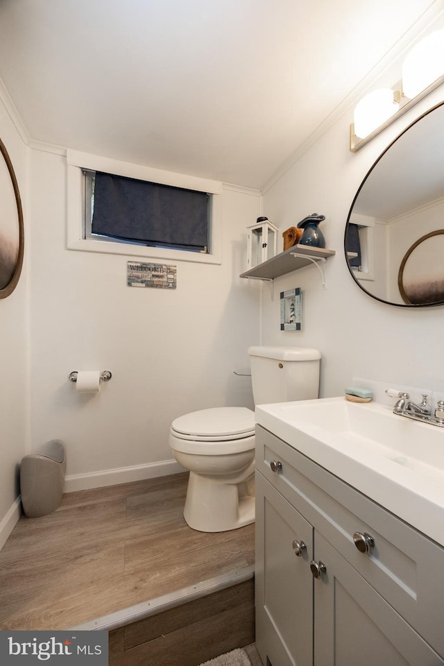 half bath featuring wood finished floors, toilet, vanity, baseboards, and ornamental molding