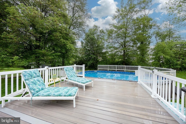 wooden terrace with view of wooded area and an outdoor pool