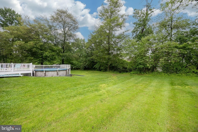 view of green lawn with an outdoor pool and a deck