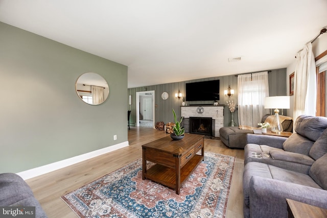 living room featuring baseboards, a brick fireplace, and light wood-type flooring