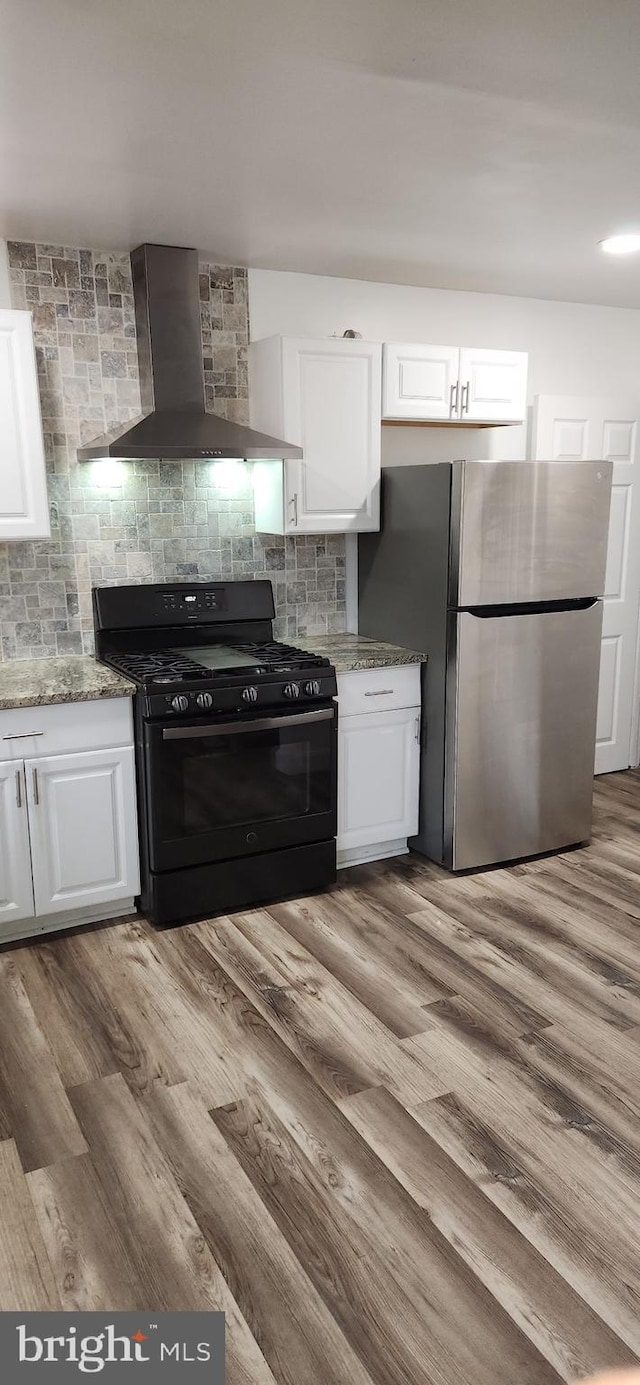 1148 Slocum St, Philadelphia, PA 19150 - kitchen featuring black range with gas cooktop, wall chimney range hood, freestanding refrigerator, white cabinets, and light stone counters