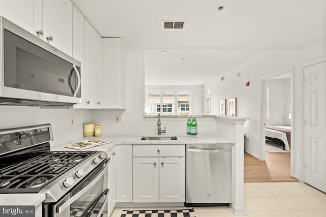 2001 12th St NW Unit 410, Washington, DC 20009 - kitchen featuring appliances with stainless steel finishes, a sink, a peninsula, white cabinets, and light stone countertops