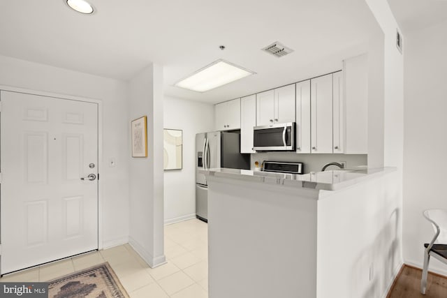 2001 12th St NW Unit 410, Washington, DC 20009 - kitchen featuring appliances with stainless steel finishes, white cabinets, baseboards, a peninsula, and light countertops