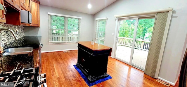 kitchen featuring a sink, decorative backsplash, light wood-style flooring, vaulted ceiling, and healthy amount of natural light
