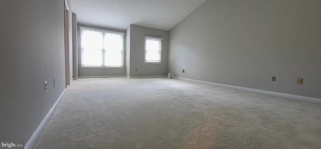 empty room featuring light carpet, lofted ceiling, and baseboards