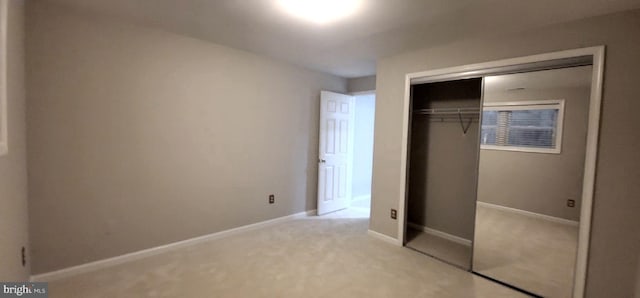 unfurnished bedroom featuring light carpet, a closet, and baseboards