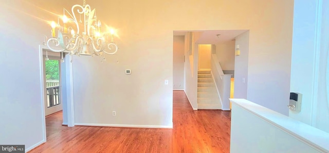 unfurnished dining area featuring wood finished floors, a chandelier, stairs, and baseboards