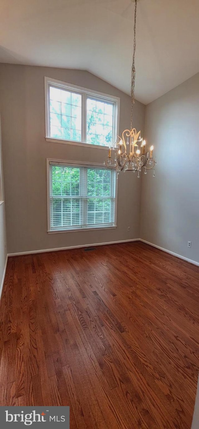 empty room with a chandelier, lofted ceiling, plenty of natural light, and wood finished floors