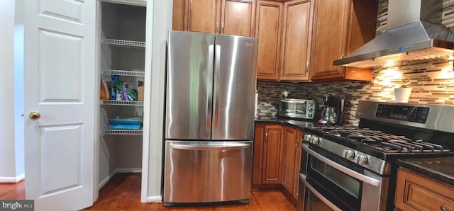 kitchen with appliances with stainless steel finishes, wall chimney exhaust hood, brown cabinetry, and wood finished floors