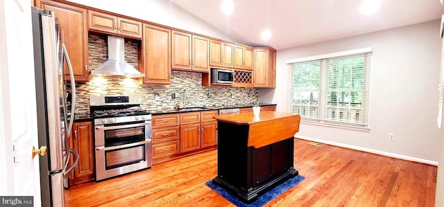 kitchen featuring appliances with stainless steel finishes, a sink, backsplash, dark countertops, and wall chimney exhaust hood