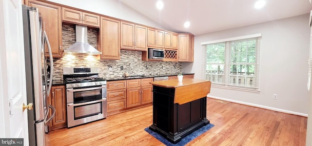 kitchen featuring stainless steel appliances, a sink, backsplash, dark countertops, and wall chimney exhaust hood