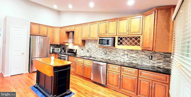kitchen featuring stainless steel appliances, wall chimney range hood, a sink, backsplash, and vaulted ceiling