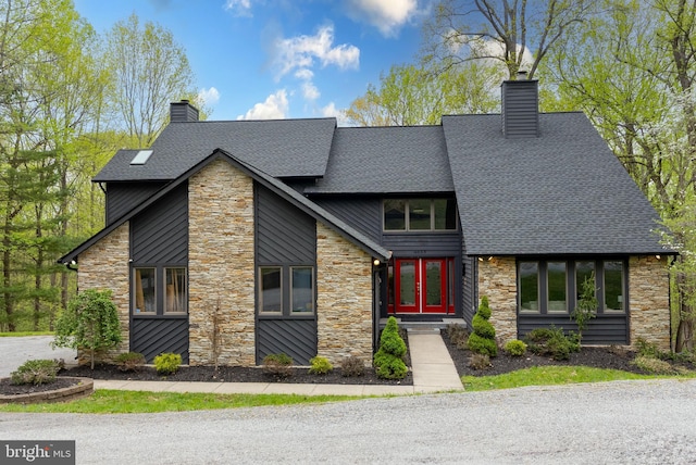 view of front of house featuring stone siding, a chimney, and roof with shingles