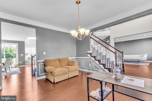 living room with stairway, a chandelier, ornamental molding, wood finished floors, and wainscoting