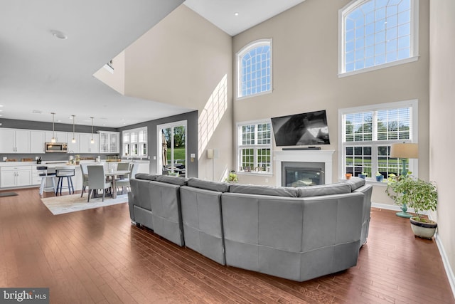 living area featuring dark wood finished floors, a glass covered fireplace, a high ceiling, and baseboards
