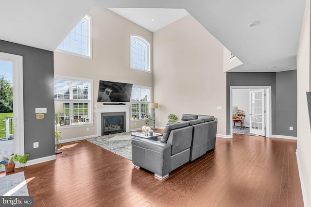 living area featuring hardwood / wood-style flooring, a fireplace with flush hearth, baseboards, and a towering ceiling