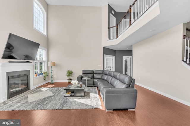 living area featuring a towering ceiling, wood finished floors, baseboards, a glass covered fireplace, and stairway