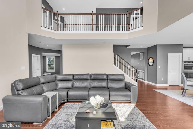 living room featuring wood finished floors, baseboards, a towering ceiling, and stairway