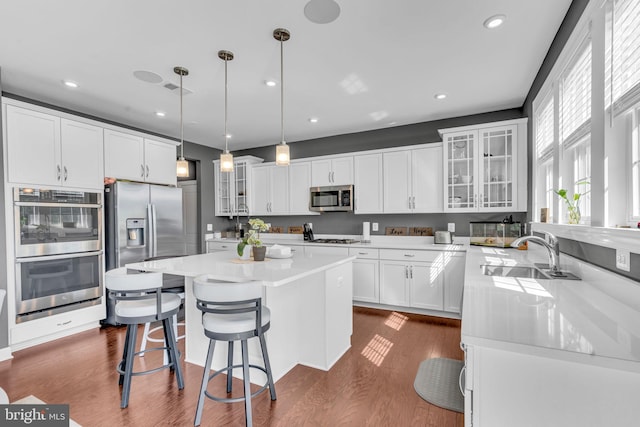 kitchen featuring appliances with stainless steel finishes, a sink, a kitchen island, white cabinetry, and recessed lighting