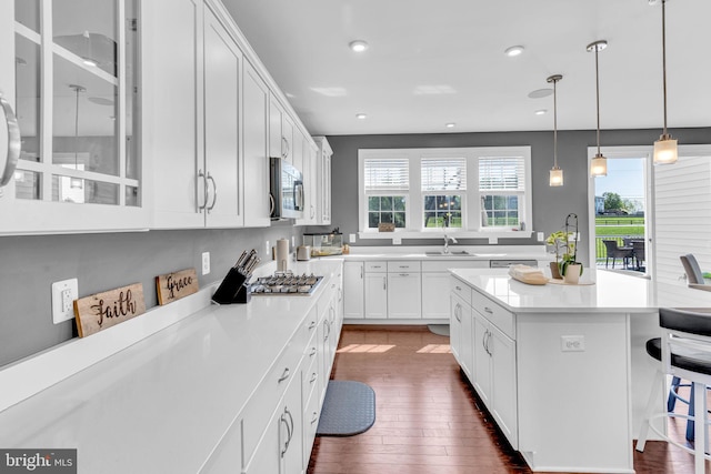 kitchen with appliances with stainless steel finishes, glass insert cabinets, dark wood-style floors, a kitchen bar, and recessed lighting