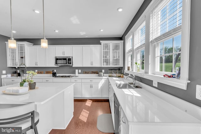 kitchen featuring appliances with stainless steel finishes, a sink, dark wood-type flooring, decorative light fixtures, and white cabinets