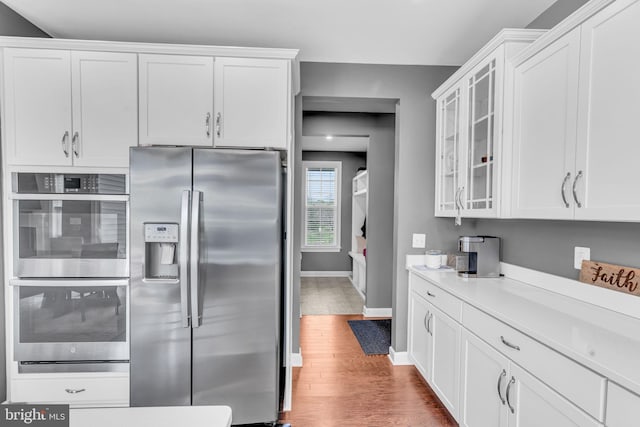 kitchen with stainless steel appliances, wood finished floors, white cabinets, and baseboards