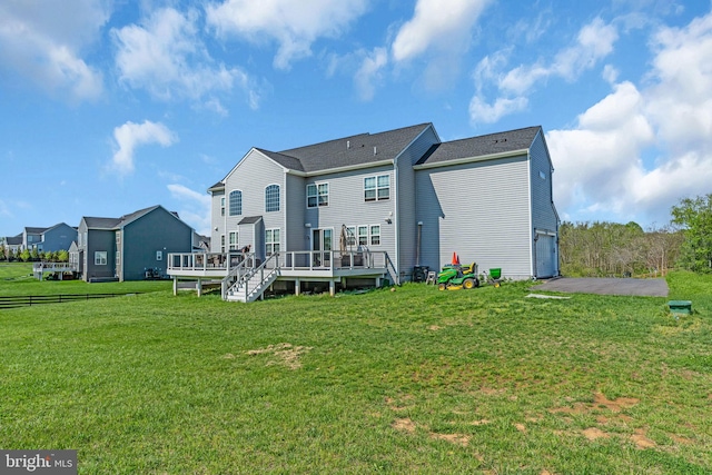 rear view of property featuring a wooden deck, an attached garage, a lawn, and asphalt driveway
