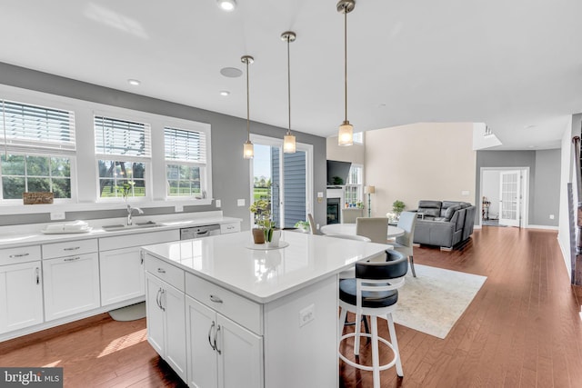 kitchen with a sink, a kitchen island, white cabinets, light countertops, and wood finished floors