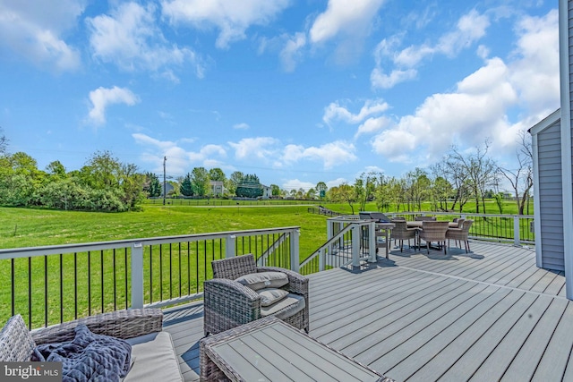 deck featuring outdoor dining space, a lawn, and a view of countryside