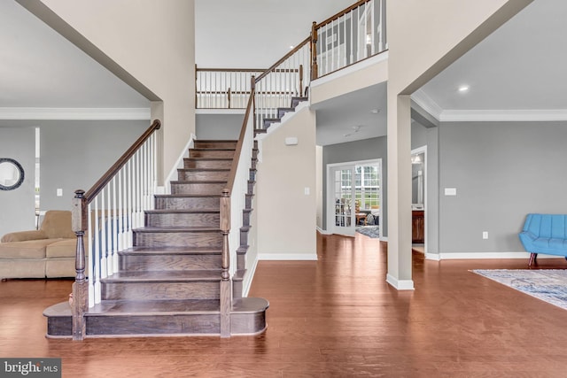 stairs with ornamental molding, wood finished floors, baseboards, a high ceiling, and recessed lighting