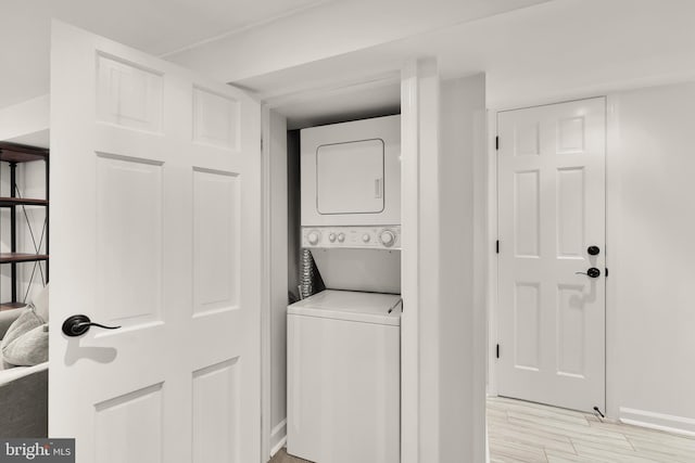laundry area featuring stacked washer / dryer, baseboards, and light wood-type flooring