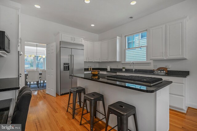 5127 Cathedral Ave NW, Washington, DC 20016 - kitchen with stainless steel appliances, white cabinets, a sink, a kitchen bar, and light wood finished floors