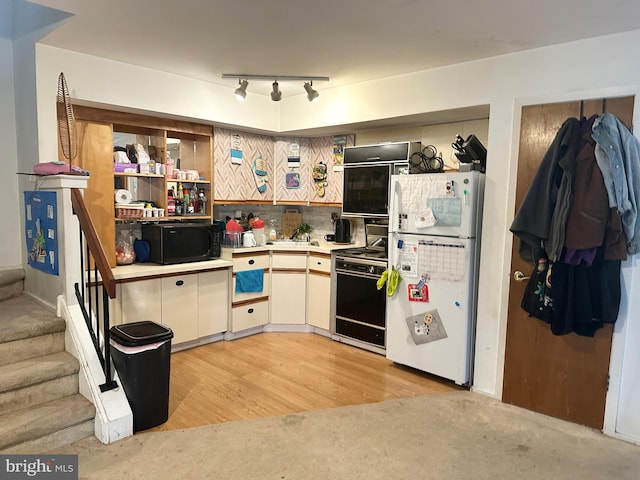 kitchen featuring freestanding refrigerator, stove, black microwave, light countertops, and light colored carpet