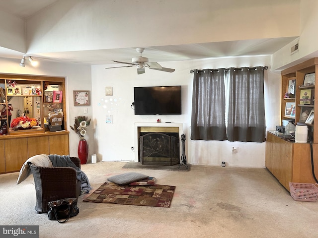 living room featuring carpet, a fireplace with raised hearth, and ceiling fan