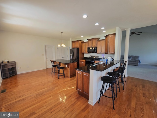 7677 Green Ridge Ln, Abbottstown, PA 17301 - kitchen with black appliances, a kitchen breakfast bar, brown cabinetry, light wood-type flooring, and recessed lighting