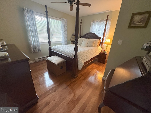 bedroom with a baseboard heating unit, wood finished floors, a ceiling fan, and baseboards