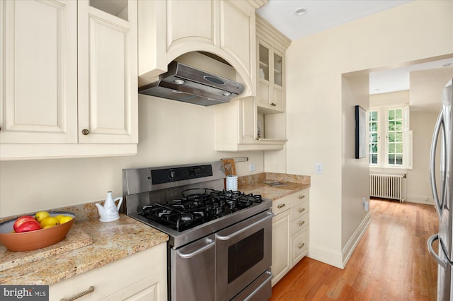 3419 Lowell St NW, Washington, DC 20016 - kitchen featuring appliances with stainless steel finishes, radiator heating unit, range hood, light wood-style floors, and cream cabinetry