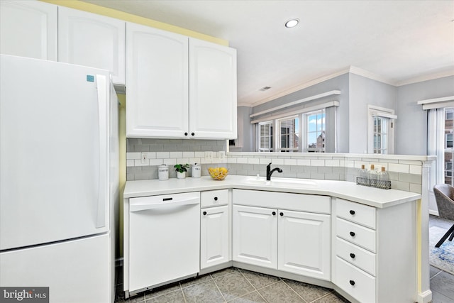kitchen featuring white appliances, a peninsula, backsplash, a sink, and crown molding