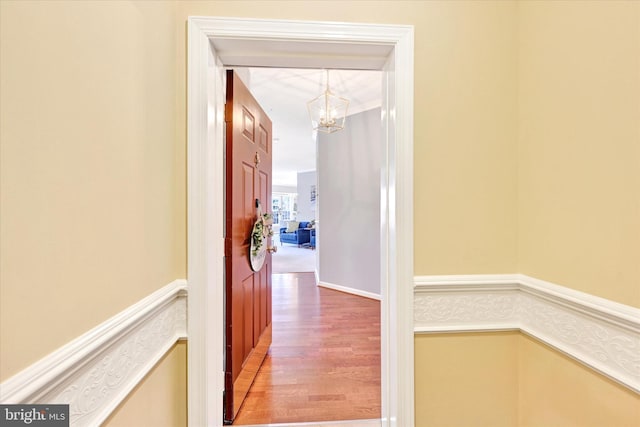 hall featuring a chandelier, wood finished floors, and wainscoting