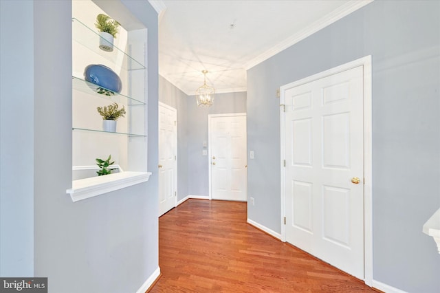 hallway with a chandelier, crown molding, wood finished floors, and baseboards