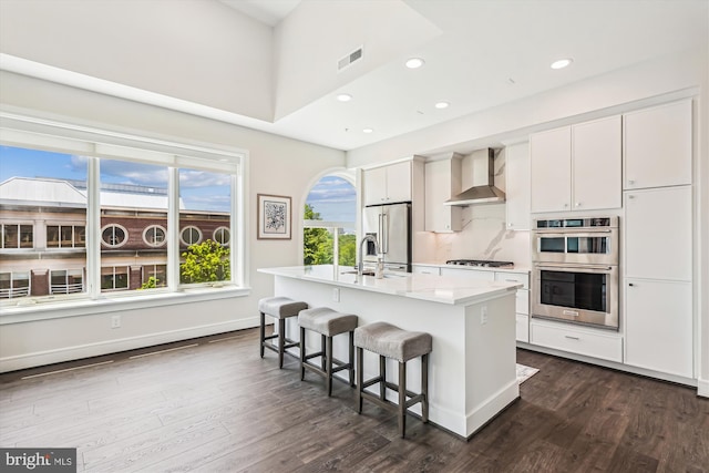 625 Slaters Ln Unit 407, Alexandria, VA 22314 - kitchen featuring wall chimney range hood, appliances with stainless steel finishes, a center island with sink, a kitchen breakfast bar, and white cabinetry