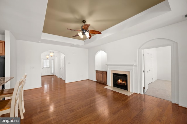 54 Ruddy Duck Ln, Bridgeville, DE 19933 - unfurnished living room featuring a tray ceiling, arched walkways, a ceiling fan, wood finished floors, and a fireplace with flush hearth