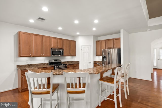 54 Ruddy Duck Ln, Bridgeville, DE 19933 - kitchen with stainless steel appliances, brown cabinetry, dark wood-style flooring, a kitchen bar, and dark stone countertops