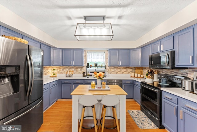 308 Fawn Dr, Winchester, VA 22602 - kitchen featuring appliances with stainless steel finishes, light wood-style flooring, a breakfast bar area, decorative backsplash, and a textured ceiling