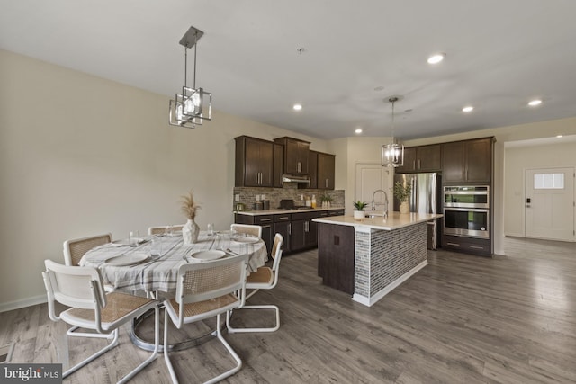 kitchen with stainless steel appliances, dark brown cabinetry, light countertops, backsplash, and under cabinet range hood