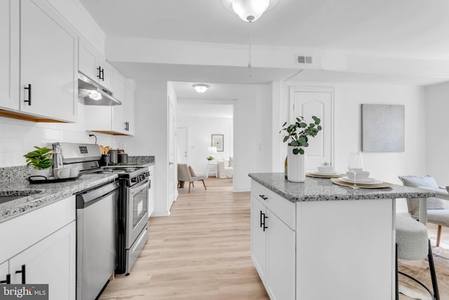 4428 Edson Pl NE, Washington, DC 20019 - kitchen with under cabinet range hood, appliances with stainless steel finishes, a kitchen breakfast bar, light wood-type flooring, and a kitchen island